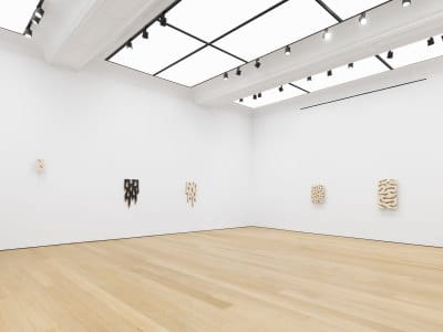 View of an art gallery exhibition with several paintings hanging on the wall.