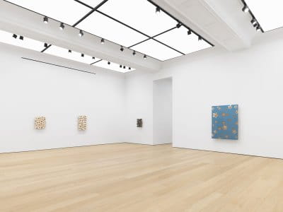 View of an art gallery exhibition with several paintings hanging on the wall.