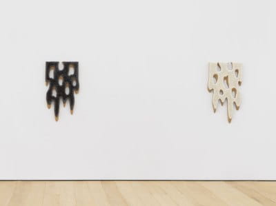 A view of two similar artworks that appear like snow sliding off a ledge. The left is in black and the right is in white.