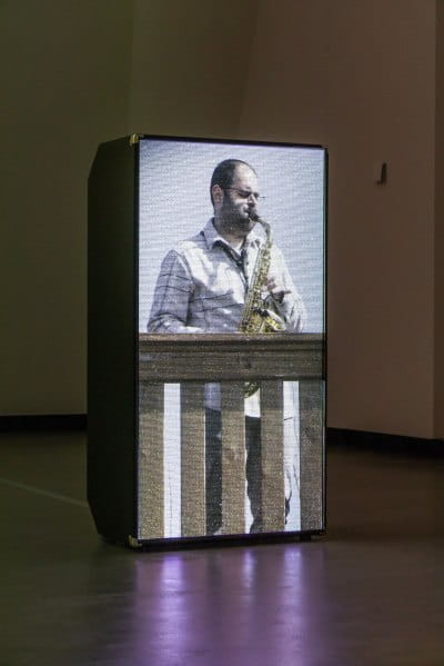 A vertical screen shows a man playing a saxophone on a balcony. 