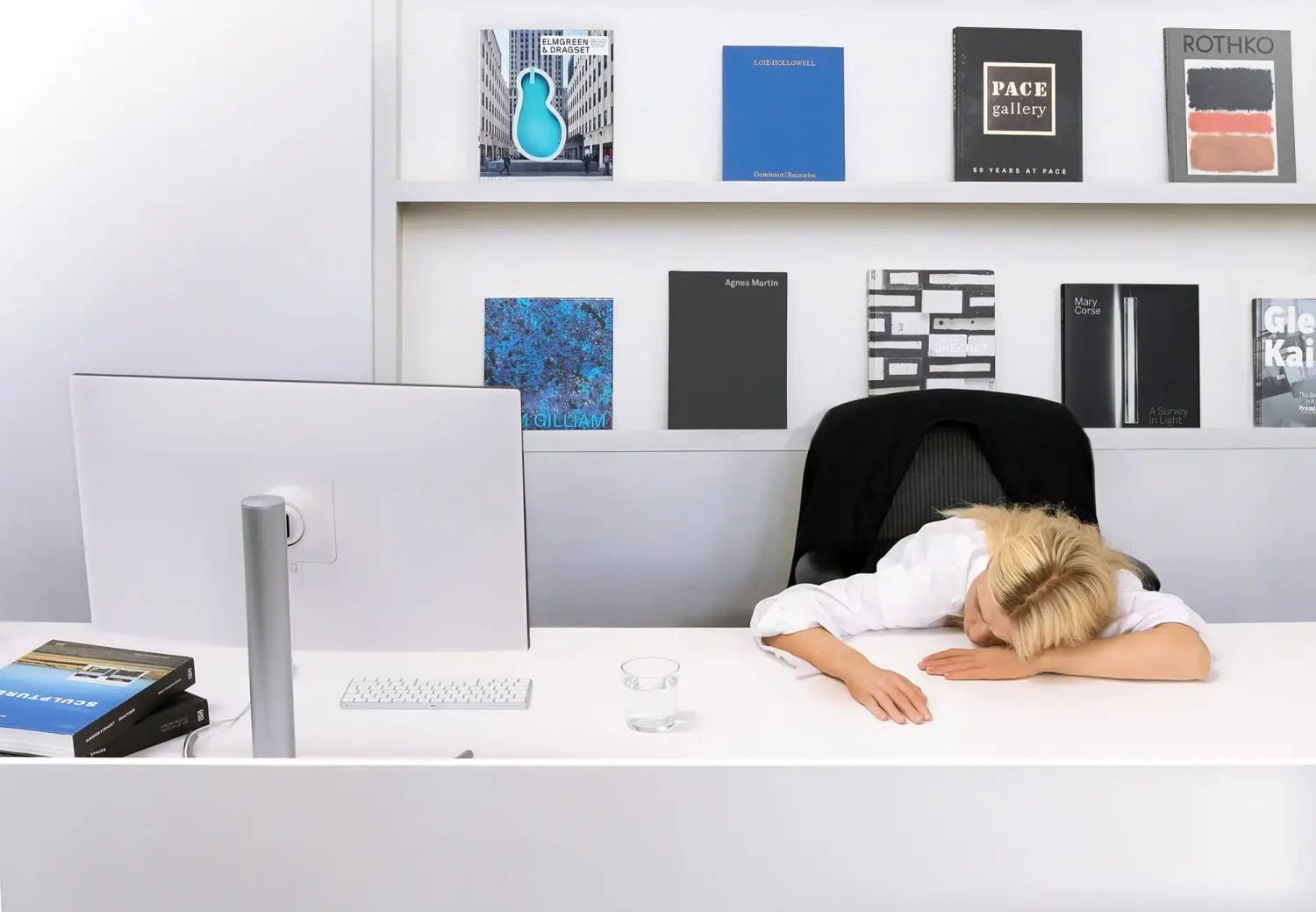 an installation by Elmgreen and Dragset of a realistic looking blond woman slumped over at her desk with a bookcase behind her