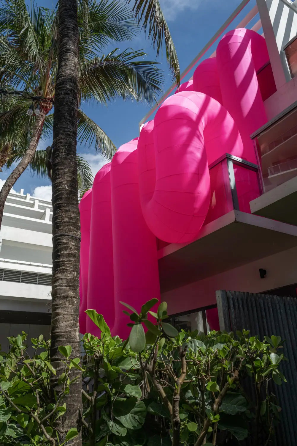 a view looking up at a large-scale inflatable sculpture by Steve Messam of an amorphous, pink form that appears to drape over a balcony
