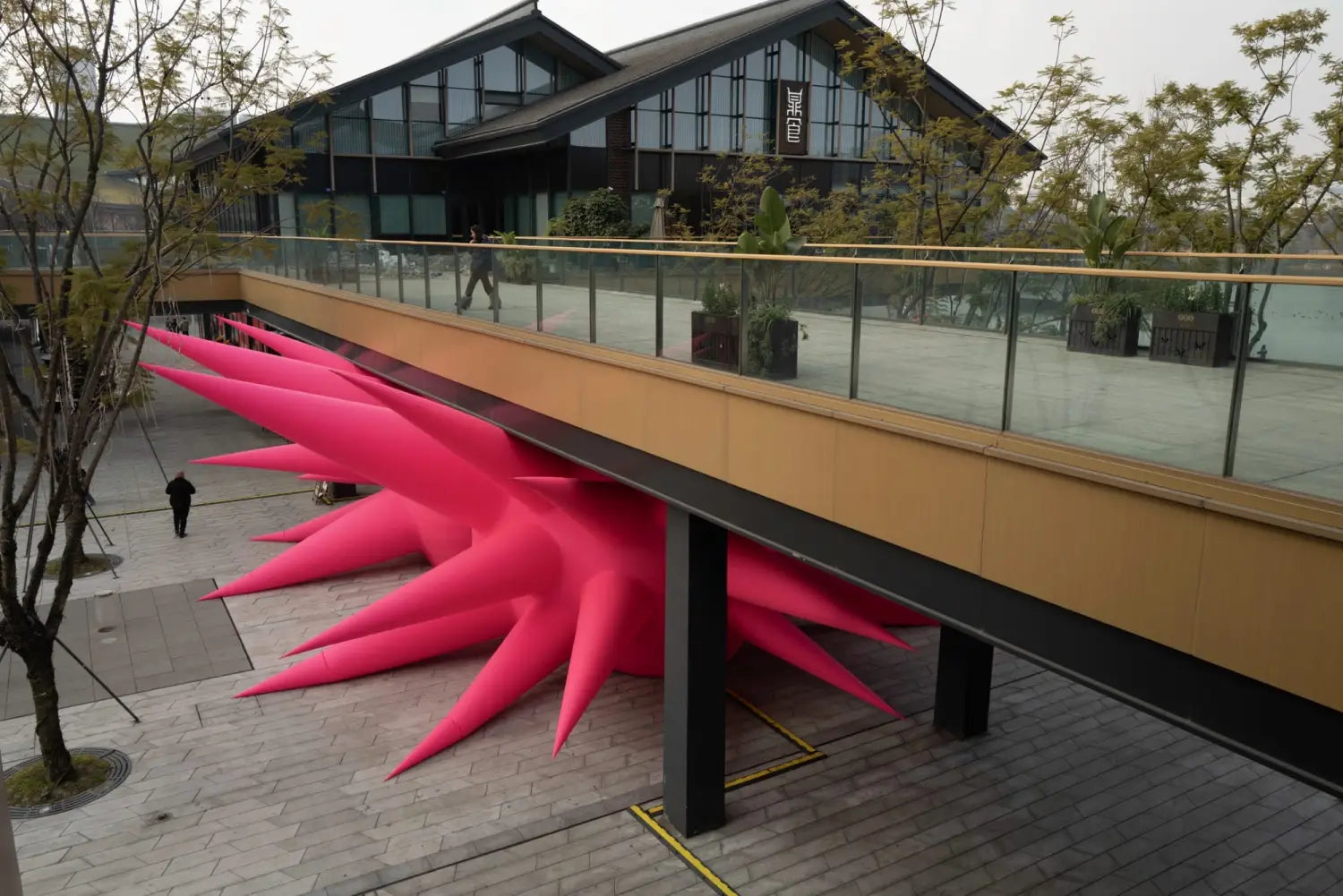 an aerial view of a large-scale inflatable sculpture installation by Steve Messam of two symmetrical, red, spiked forms wedged under a bridge