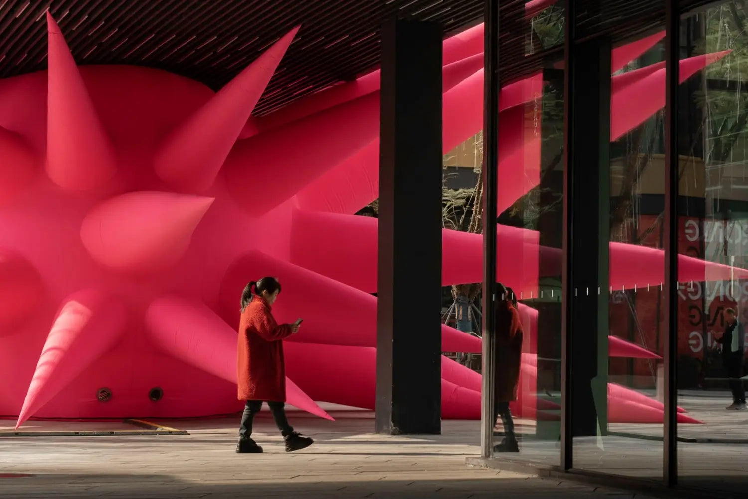 a woman walks in front of a large-scale inflatable sculpture installation by Steve Messam of ared, spiked form wedged under a bridge