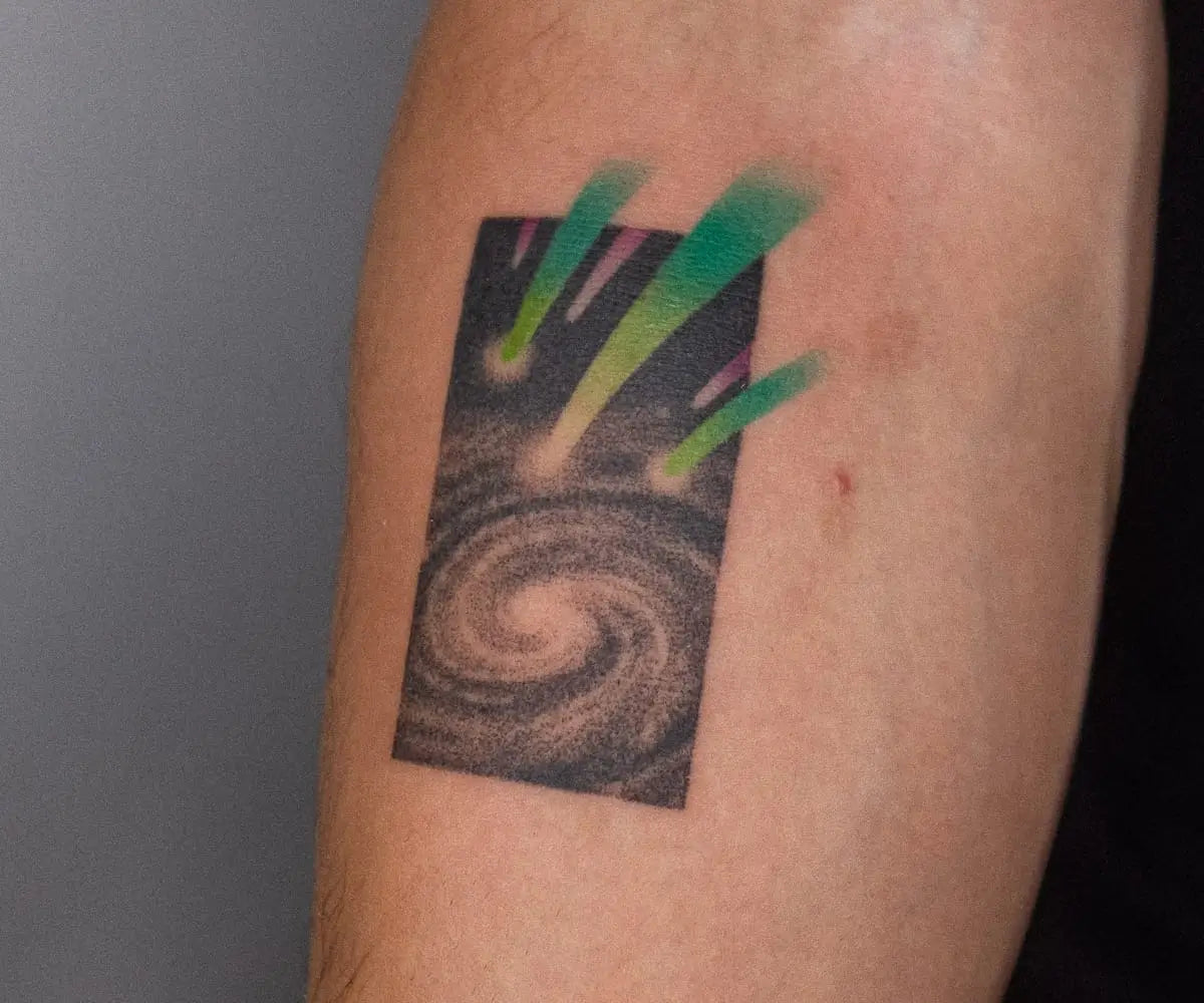 a white arm with a tattoo by Nano Ponto of a trio of green comets shooting from a galaxy