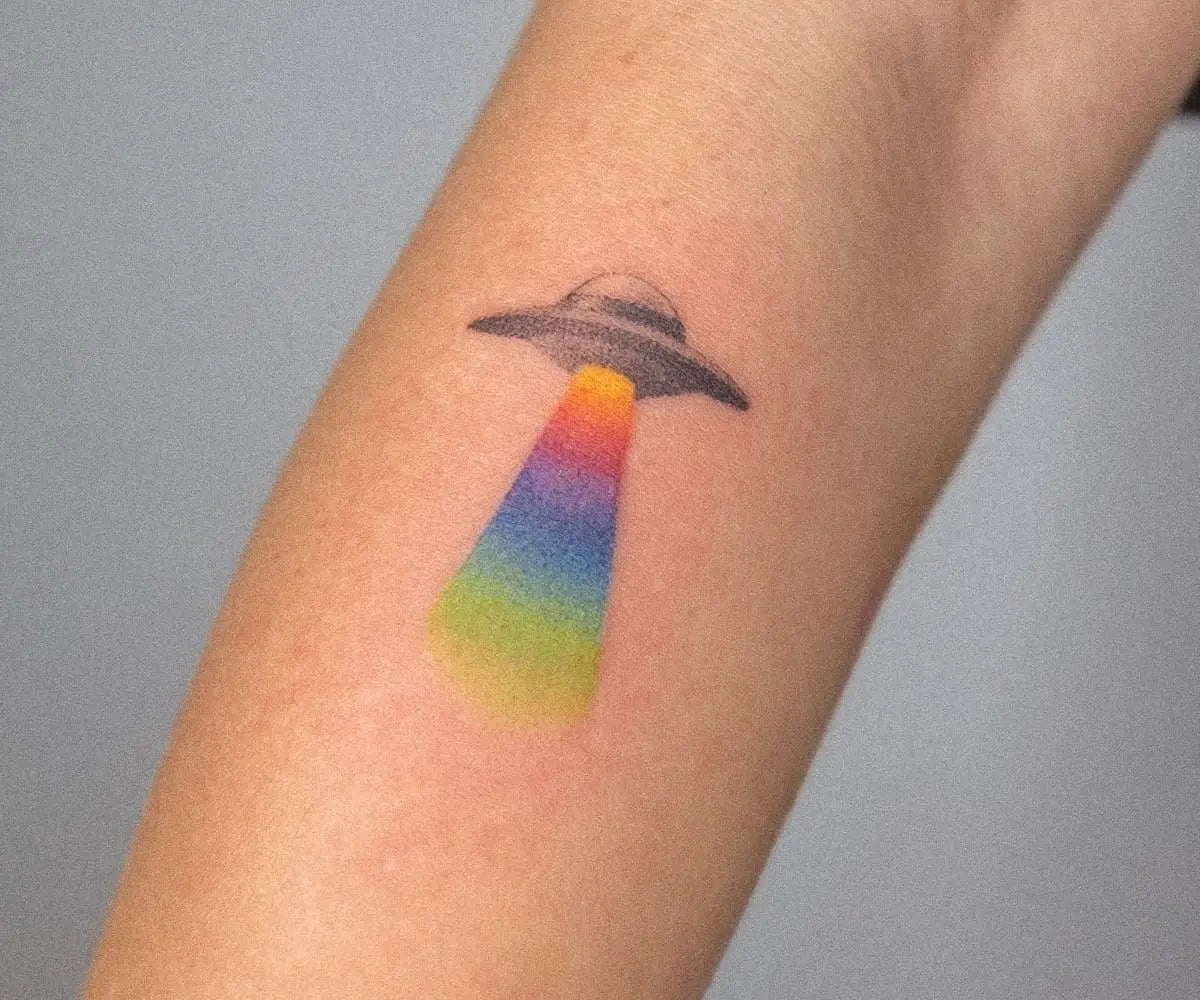 a white arm with a tattoo by Nano Ponto of a vibrant gradient beaming from a flying saucer