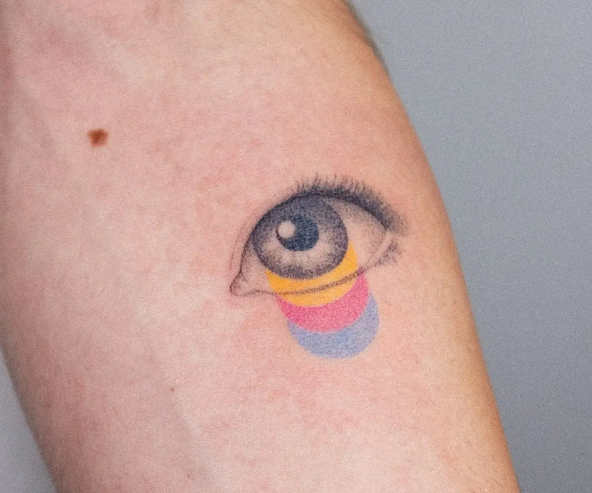 a white arm with a tattoo by Nano Ponto of a vibrant gradient crying from a black and white eye